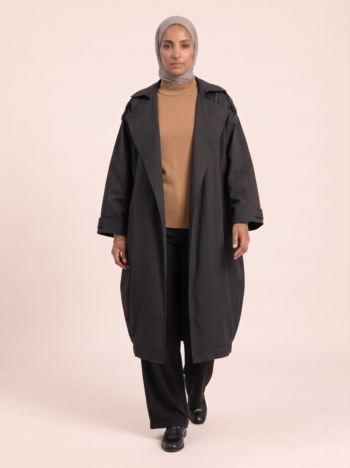 Trench oversize noir porté ouvert sur un pull col roulé camel et un pantalon large noir
